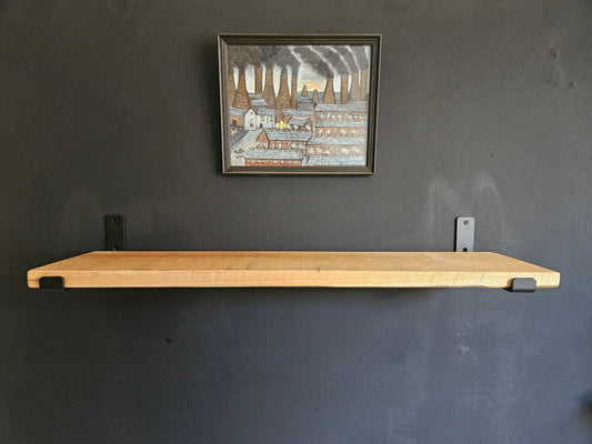 Wooden shelf mounted on a dark gray wall with a framed picture above it. Shelf made of pine scaffolding board