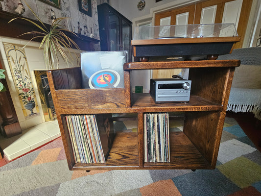 A dark oak vinyl storage unit featuring a sleek design with dedicated space for an amplifier, ample storage for vinyl records, and a convenient flicking bin for easily accessing and browsing through albums, adding elegance and functionality to any music area