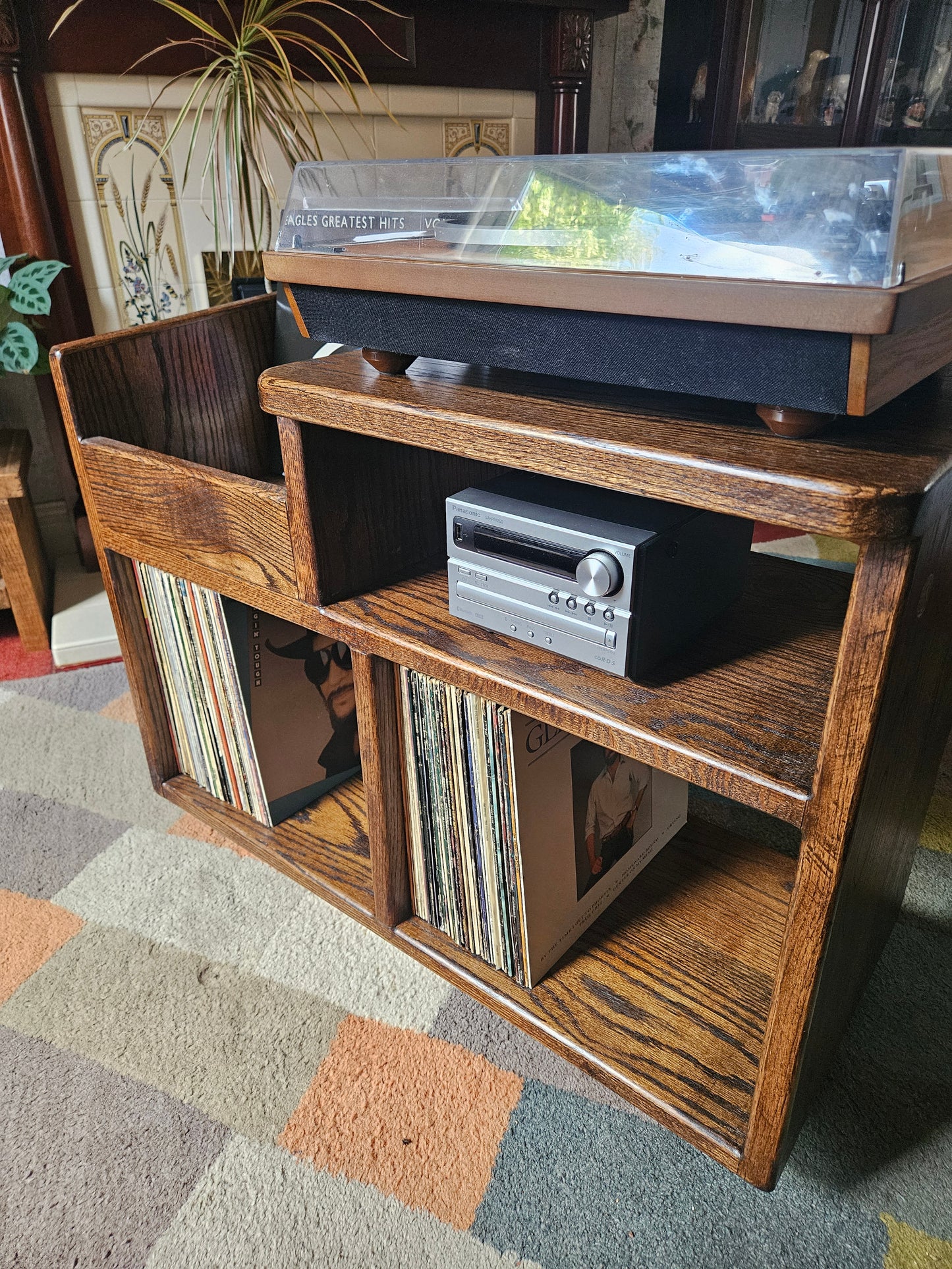 A dark oak vinyl storage unit featuring a sleek design with dedicated space for an amplifier, ample storage for vinyl records, and a convenient flicking bin for easily accessing and browsing through albums, adding elegance and functionality to any music area