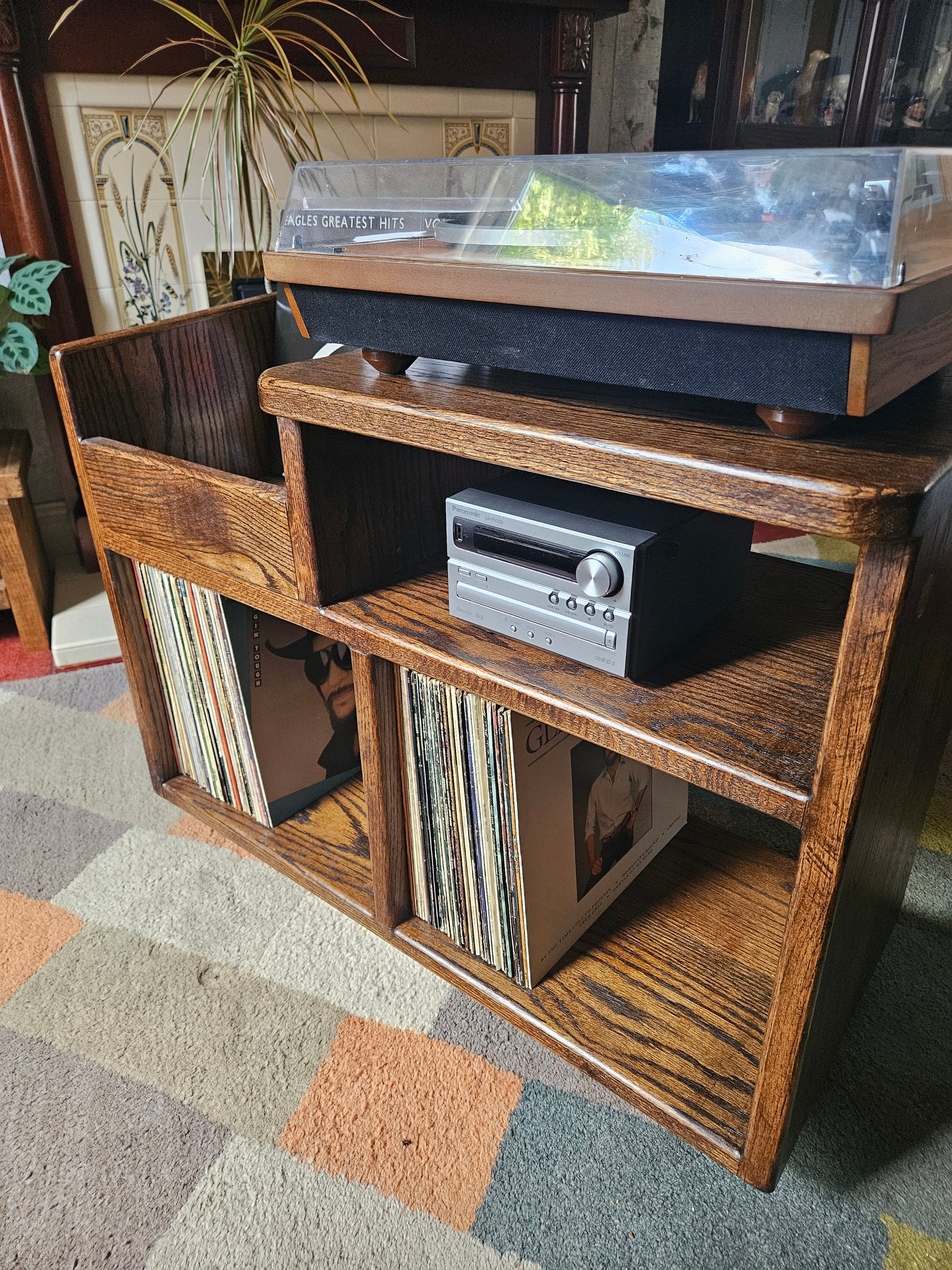 A dark oak vinyl storage unit featuring a sleek design with dedicated space for an amplifier, ample storage for vinyl records, and a convenient flicking bin for easily accessing and browsing through albums, adding elegance and functionality to any music area