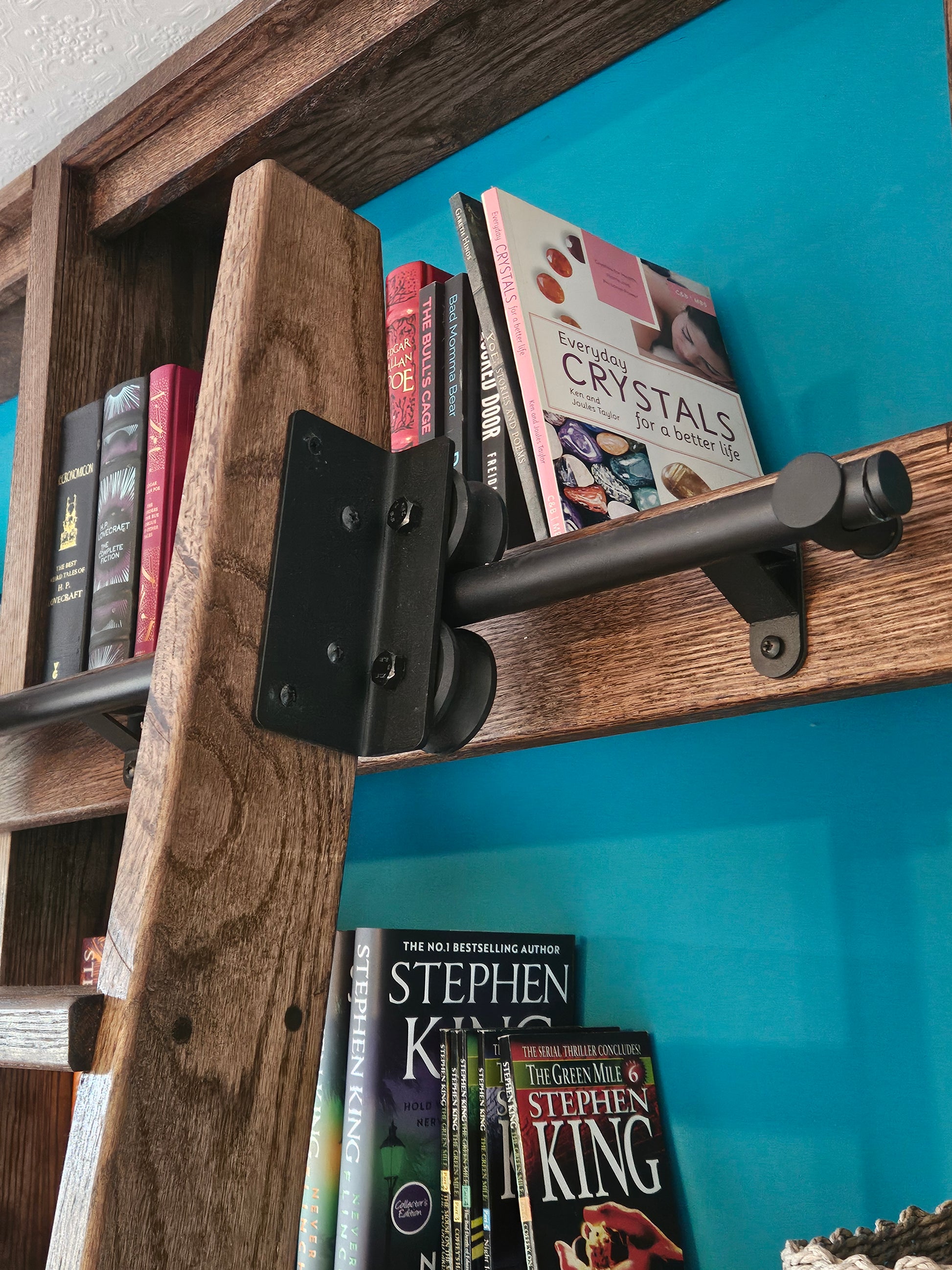 Wooden shelf with books and a black bracket against a blue wall, Close up of the rolling sliding ladder mechanism